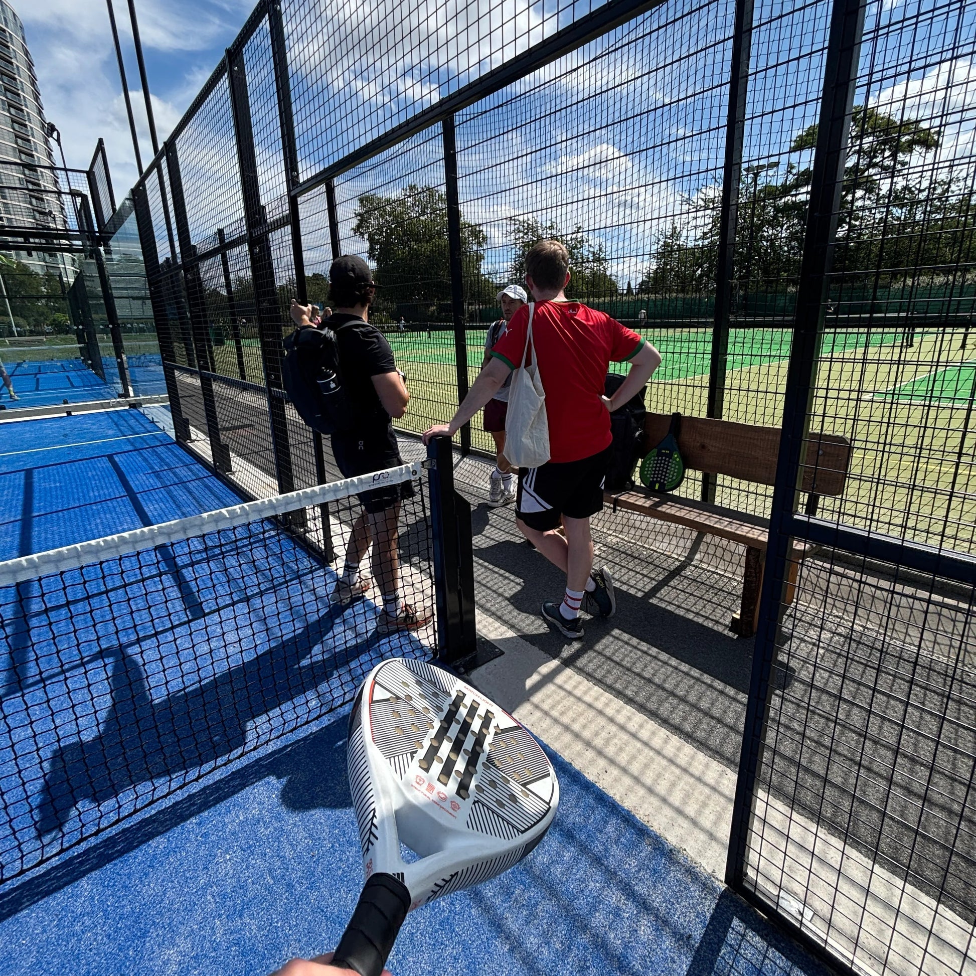 People playing paddle tennis on a blue court with a clear sky.
