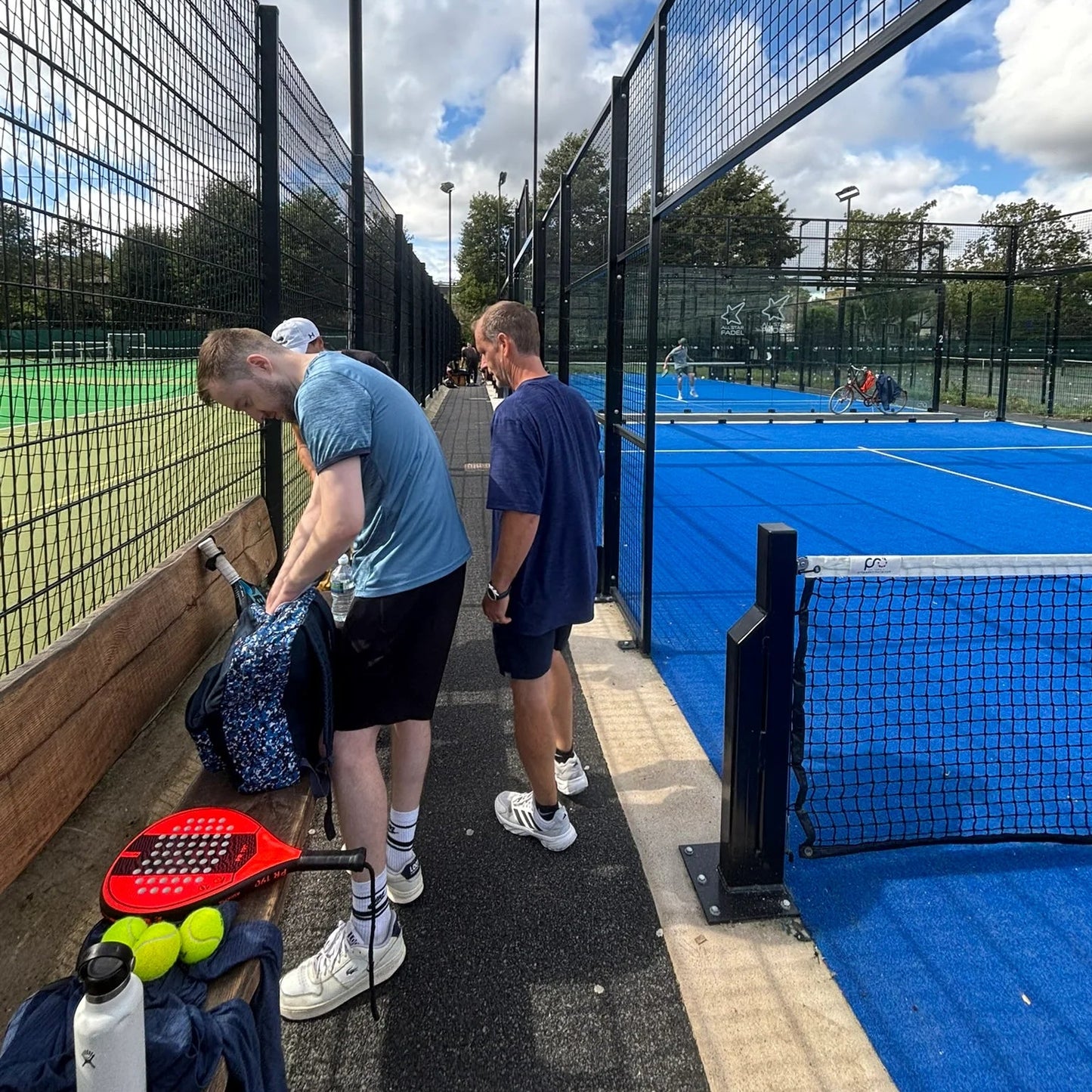 Two men on a blue padel tennis court with sports equipment.