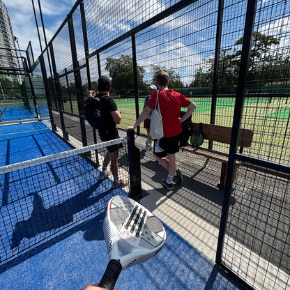 People playing paddle tennis on a blue court with a clear sky.
